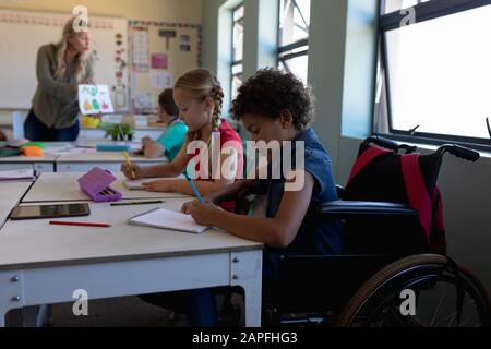 Une écolière assise dans un fauteuil roulant dans une salle de classe de l'école primaire Banque D'Images