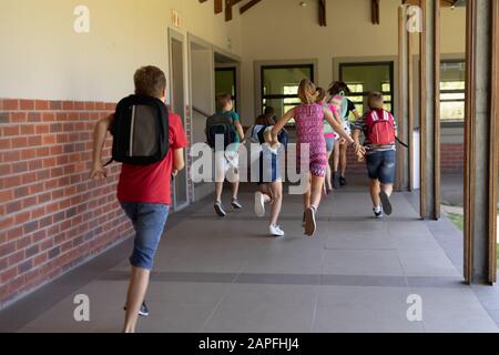 Groupe d'écoliers s'exécutant dans un couloir extérieur à l'école primaire Banque D'Images