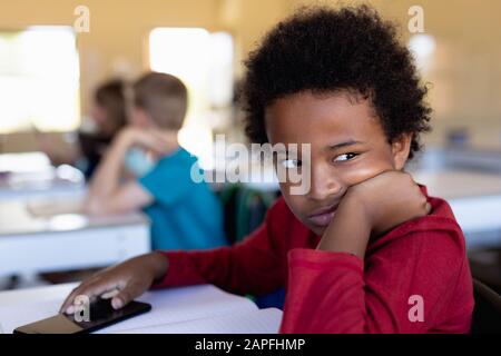 Un écolier se penchant sur sa main dans une salle de classe de l'école primaire Banque D'Images