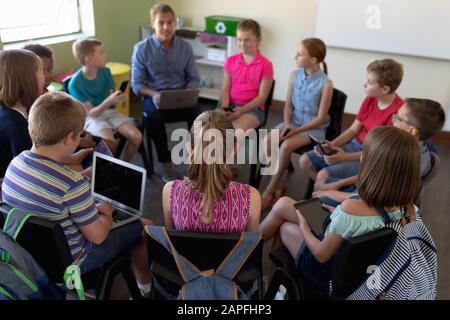 professeur d'école masculine assis sur une chaise dans un cercle avec un groupe d'écoliers Banque D'Images