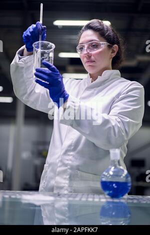Une jeune fille de laboratoire dans des verres et un manteau blanc avec du verre expérimental dans ses mains mène des expériences sur fond démoqué Banque D'Images