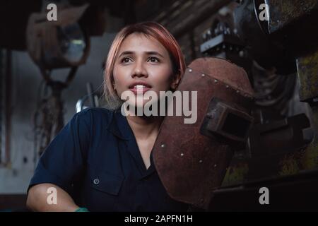 Ingénieur industriel féminin diversifié tenant un casque de soudage après un poste de travail - jeune ouvrier asiatique en métal d'usine prenant une pause - apprenti hispanique femme, apprenant de nouvelles compétences en formation de stage Banque D'Images