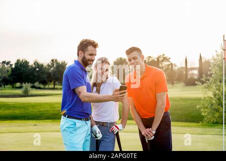 Amis lisant un message texte sur un smartphone sur un parcours de golf Banque D'Images