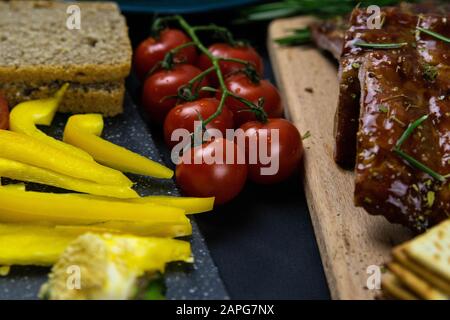 Côtes sous sauce au miel sur une planche en bois à côté des tomates, du papier cloche et du pain. Vues de dessus Banque D'Images