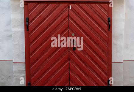 Grande porte en bois rouge avec poignées et charnières forgées noires dans un bâtiment ancien. Banque D'Images