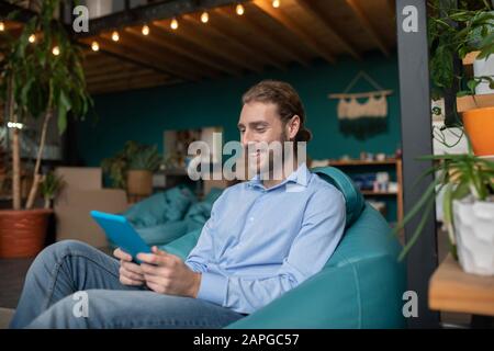 Homme souriant assis dans un fauteuil et utilisant une tablette Banque D'Images