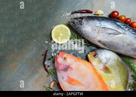 Poisson frais avec des épices et herbes de romarin citron tomate ail pour la nourriture cuite / poisson cru Thon tilapia rouge et pomfret poisson sur fond de plaque sombre Banque D'Images