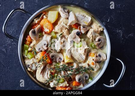 ragoût traditionnel de poulet cuit lentement avec légumes et sauce crémeuse dans une casserole sur une table en béton, vue horizontale de dessus, plat, gros plan Banque D'Images