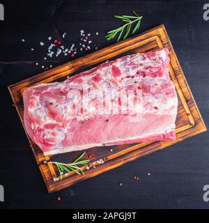 Gros morceau entier de viande de porc avec assaisonnement sur hacher planche sur fond noir Banque D'Images