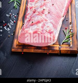Gros morceau entier de viande de porc avec assaisonnement sur hacher planche sur fond noir Banque D'Images