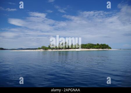 Une petite île avec une plage de sable, surcultivée avec des palmiers. Calme mer sur une journée ensoleillée avec peu de nuages dispersés dans le ciel. Banque D'Images