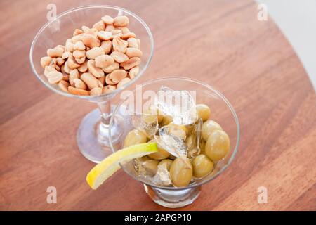 Les olives vertes au citron et à la glace et les arachides dans les verres se tiennent sur une table ronde en bois, apéritif gratuit dans un bar, vue sur le dessus Banque D'Images