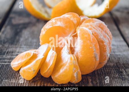 La mandarine pelée mûre sans peau se trouve sur la table à côté de morceaux de mandarine mûre. Citruses mandarines ou oranges. Gros plan. Banque D'Images