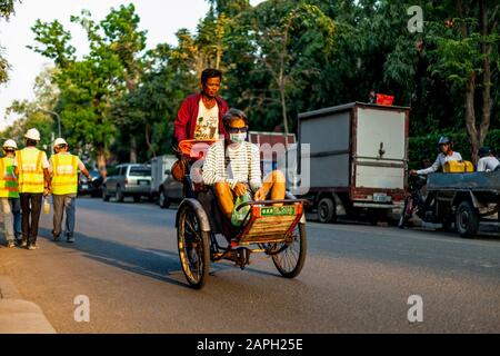 Un chauffeur de cyclo khmer pédante un cyclo alors qu'un passager masculin est assis dans le siège d'une rue de ville connue sous le nom de ligne d'art dans la ville de Phnom Penh, au Cambodge. Banque D'Images