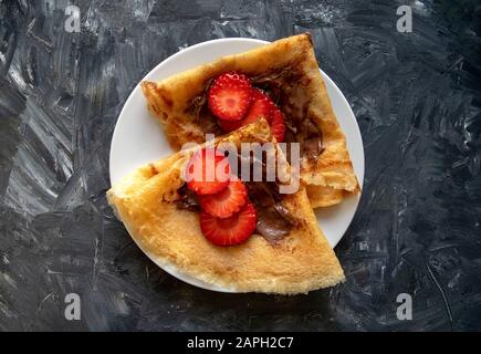 Crêpes fraîches avec pâte de chocolat et fraise sur fond gris. Vue de dessus. Crêpes de style russe pour la semaine Pancake. Banque D'Images