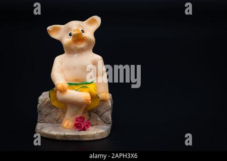 Figurine d'un petit porc assis sur un banc, fond noir Banque D'Images