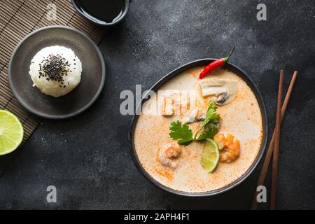 Tom Yam kung soupe thaï aux crevettes, fruits de mer, le lait de coco, le piment et le riz en noir bol. Vue de dessus. Orientation horizontale. C'Asie Banque D'Images