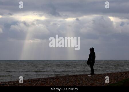 Une femme qui s'est promenée sur la plage de galets en regardant dehors pour voir sous le ciel orageux, Hastings, East Sussex, Angleterre. Banque D'Images