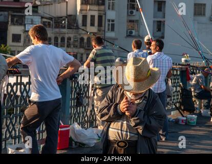 Istanbul / Turquie vieux homme portant chapeau de paille allume une cigarette sur le pont de Galata. Plusieurs pêcheurs en arrière-plan. Banque D'Images
