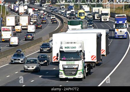 En regardant vers le bas sur la circulation en marche arrière sur l'autoroute M25, très fréquentée, derrière deux camions chargés de grandes charges, un bâtiment modulaire surdimensionné, Angleterre Royaume-Uni Banque D'Images