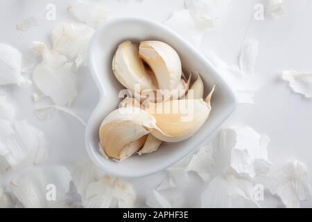 studio avec photo de gousses d'ail individuelles dans un bol en forme de coeur sur des galets sur fond blanc Banque D'Images