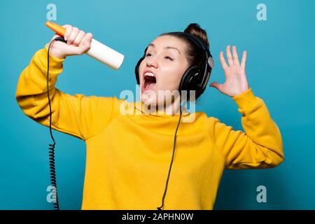 une jeune fille lumineuse dans un grand casque écoute la musique et chante émotionnellement le long du rouleau de vêtements Banque D'Images