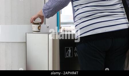 une vieille femme jetant une tasse de papier sur la poubelle à l'intérieur d'un aéroport en allemagne. Banque D'Images