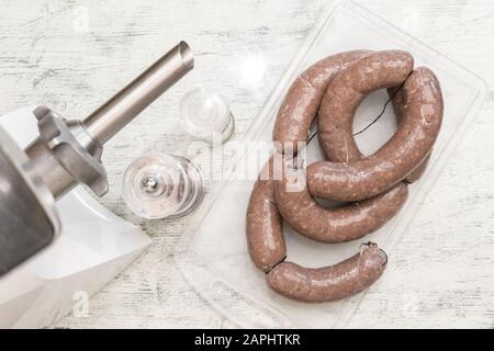 Les saucisses de bœuf crues faites maison, étroitement liées aux filets, se trouvent sur la planche à découper en plastique. Accessoire de mouture de viande métallique pour la cuisson de viande hachée. Santé f Banque D'Images