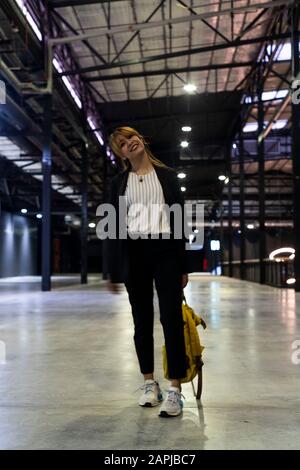 Blonde femme cheveux avec demi-lié et la coiffure de la frange marchant dans le bourreau après visite de son client, elle est heureuse et sourire et tenir le backpa jaune Banque D'Images