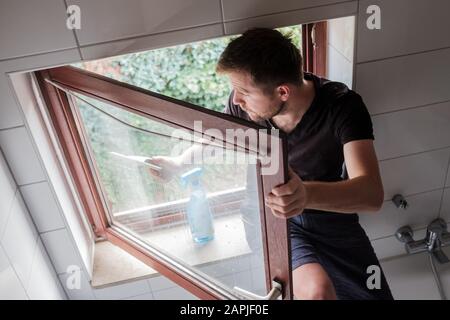 Un homme caucasien lave une fenêtre dans une maison à l'aide d'un grattoir Banque D'Images