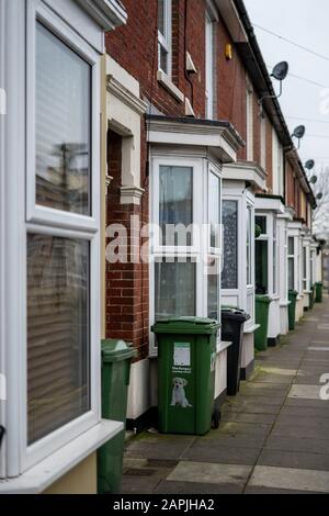 L'extérieur des maisons en terrasses en briques anglaises typiques avec des poubelles à roues vertes à l'avant Banque D'Images