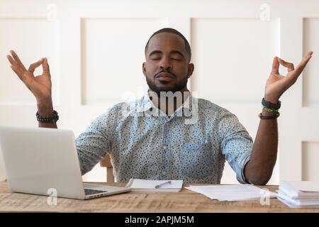 Homme africain assis au bureau méditant pendant la journée de travail sur le lieu de travail Banque D'Images