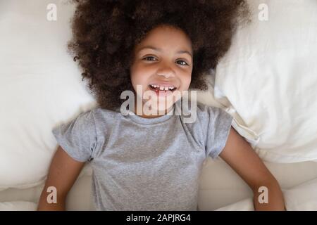 Petite fille africaine se trouve dans le sourire de lit regardant l'appareil photo Banque D'Images