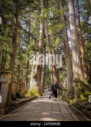 Koyasan, JAPON - Mai 2019: Moine marchant sur le long chemin de 2 km avec des tombes anciennes dans le cimetière d'Okunoin vers le mausolée de Kobo daishi Banque D'Images