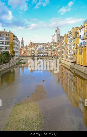 Gérone, Catalogne, Espagne, maisons jaunes et oranges colorées et autres bâtiments reflétés dans l'eau de la rivière Onyar, l'église de Sant Feliu et Saint Mary Banque D'Images