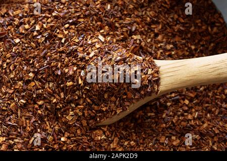 Gros plan (macro) de rooibos ou de feuilles de thé de brousse; soulevé d'un bol avec une cuillère en bois. Banque D'Images