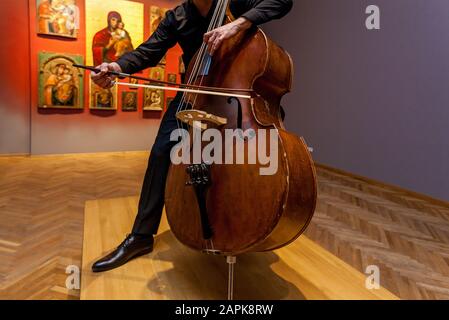 Ukraine Kiev 9 avril 2019: Un musicien avec une basse double dans un costume sombre jouant sur le fond d'un mur. Banque D'Images