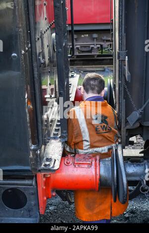 Vue arrière du membre d'équipage du train à vapeur, ouvrier, reliant la locomotive britannique ancienne au train ferroviaire, sur la voie de la gare historique de Severn Valley. Banque D'Images