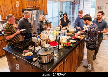 La famille s'est rassemblée autour de l'île du centre de cuisine pour un dîner de Thanksgiving de style buffet Banque D'Images