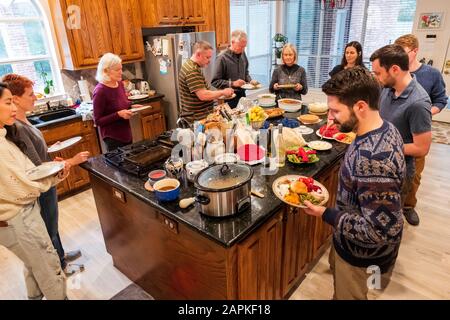 La famille s'est rassemblée autour de l'île du centre de cuisine pour un dîner de Thanksgiving de style buffet Banque D'Images