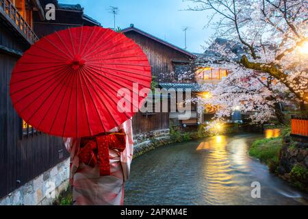 Une jeune femme asiatique qui porte un kimono traditionnel japonais avec un parapluie rouge à visiter à la célèbre destination cerisier fleuris à Shirakawa River Banque D'Images