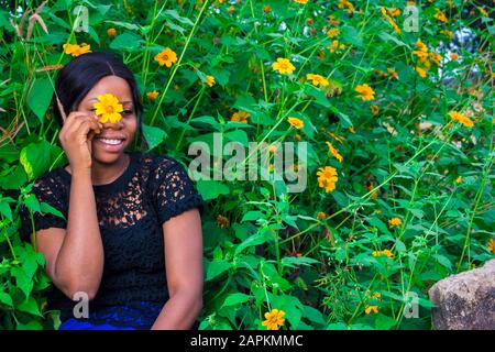 belle jeune femme africaine tenant un arbre marigold tournesol couvrant son visage et souriant Banque D'Images