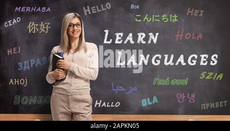 Jeune professeur de langue féminine debout devant un tableau noir avec bonjour écrit dans différentes langues Banque D'Images