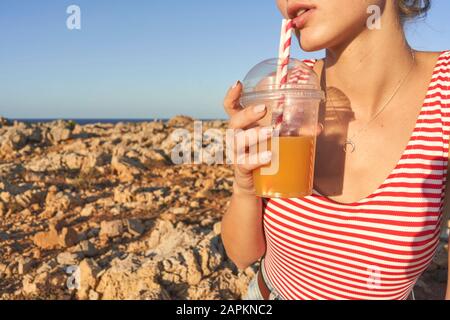 Jeune femme buvant du jus sur la plage rocheuse Banque D'Images