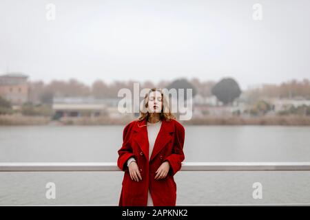 Portrait de la jeune femme portant un manteau rouge, se penchant sur la rampe pendant la journée des pluies Banque D'Images