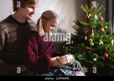 Blonde fille assise sur les genoux du père et ouverture cadeau de Noël Banque D'Images