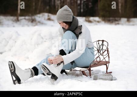 Femme souriante mettant sur des patins à glace sur le champ de neige Banque D'Images