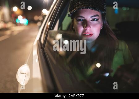 Femme assise sur l'arrière d'une voiture dans la ville la nuit Banque D'Images