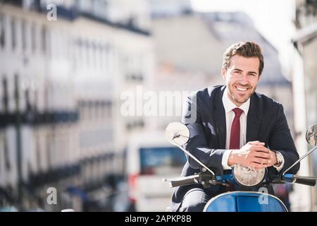 Portrait de jeune homme d'affaires souriant sur scooter automobile dans la ville, Lisbonne, Portugal Banque D'Images