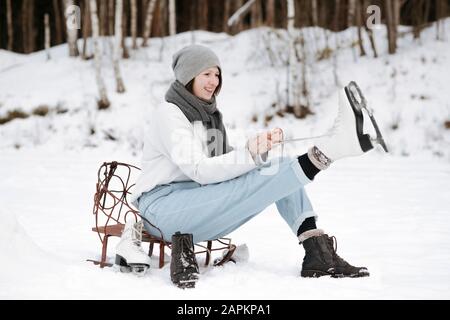 Portrait d'une femme souriante mettant des patins à glace sur le champ de neige Banque D'Images